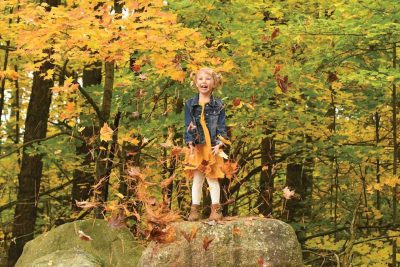 Recomended Article: Hodag Country quick fall color guide | Girl standing on a large rock throwing leaves at Almon Park in Autumn