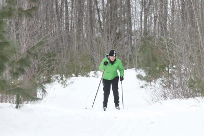 Recomended Article: Two great ski trails to try | Women in green coat cross-counrty skiing the Cavoc Trails